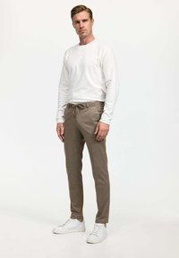 Chemise blanche à manches longues et pantalon à cordon à la taille de couleur marron clair, présentant un tissu texturé et une coupe ajustée, portés avec des baskets blanches.