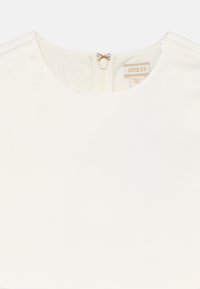 Λευκό φόρεμα με στρογγυλή λαιμόκοψη και φερμουάρ στην πλάτη, με εμφανές εσωτερικό ετικέτα της μάρκας Guess στο γιακά.