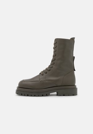 Bottes militaires à lacets en cuir vert foncé avec un bout rond et une semelle en caoutchouc robuste. Caractéristiques : détails de couture et languette de tirage.