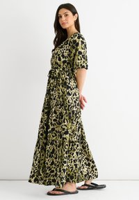 Maxi dress in green and black animal print, short sleeves, belted waist, tiered design, lightweight fabric, worn with black flip-flops.