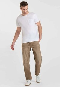 T-shirt en coton blanc avec poche, associé à un pantalon en denim marron clair affichant une texture lisse et des détails de couture subtils, complété par des baskets blanches.