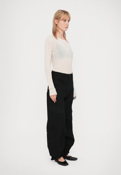 Calças cargo pretas com bolsos laterais, combinadas com uma blusa de manga longa em bege claro. A blusa tem um formato justo e o tecido parece macio e transparente.