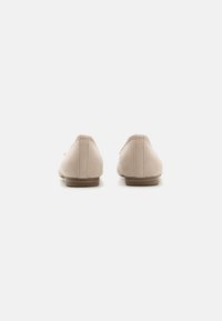 Chaussures en daim beige avec un petit talon rond et un design simple. Couture visible le long de l'arrière et silhouette minimaliste.