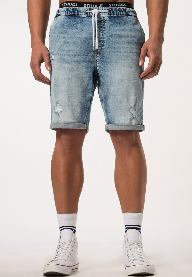 Lichtblauwe denim shorts met een versleten ontwerp, omgerolde mouwen, een tailleband met trekkoord en een logo tailleband. Witte sneakers met blauwe accenten.