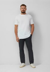 Biały t-shirt z krótkim rękawem w połączeniu z ciemnoszarymi spodniami i białymi sneakersami z beżową podeszwą. Prosty fason i luźne dopasowanie.