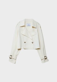 Veste courte de couleur crème avec larges revers, boutons croisés, manches longues et sangles à boucles aux poignets sur fond blanc.