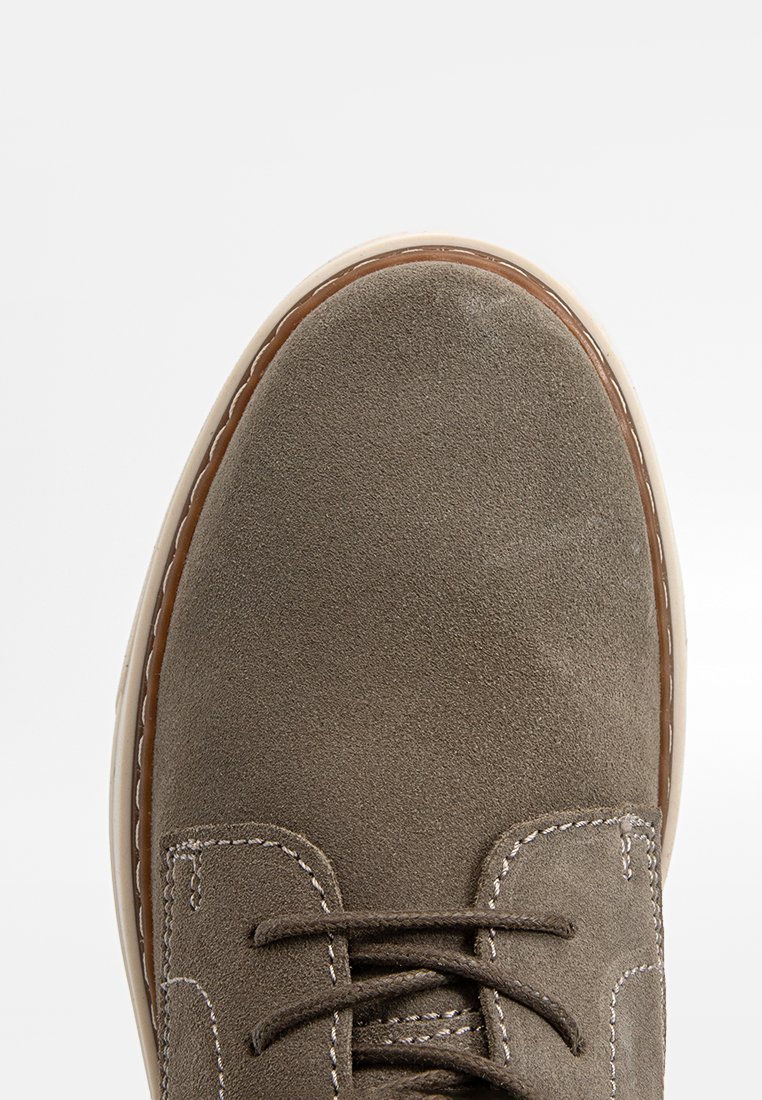 Graue Wildlederschuhe mit abgerundetem Zehenbereich, kontrastierenden weißen Nähten und einer leichten Gummisohle. Die Schnürsenkel sind zentral angebracht; minimalistische Gestaltung.