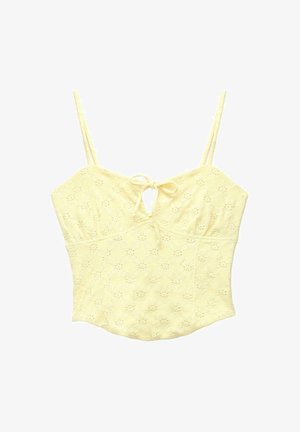 Žlutý krajkový crop top s tenkými ramínky a malou mašlí uvázanou u výstřihu, s jemným květinovým vzorem.