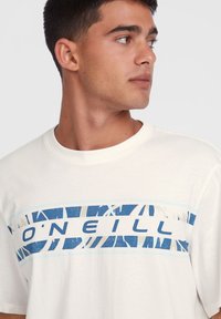 Kortærmet, cremet bomulds T-shirt med et blåt grafisk design og teksten "O'Neill" tværs over brystet. Klassisk crew neck stil.