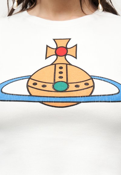 Πορτοκαλί και μπλε στυλιζαρισμένη σφαίρα με σχεδιασμό δακτυλίου και σταυρού, τυπωμένη σε λευκό ύφασμα, τοποθετημένη στο κέντρο του άνω μέρους του θώρακα ενός ατόμου.