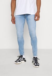 Vaqueros pitillo de mezclilla azul claro, con un diseño clásico de cinco bolsillos y un ligero desgaste. Combinados con zapatillas negras y blancas.