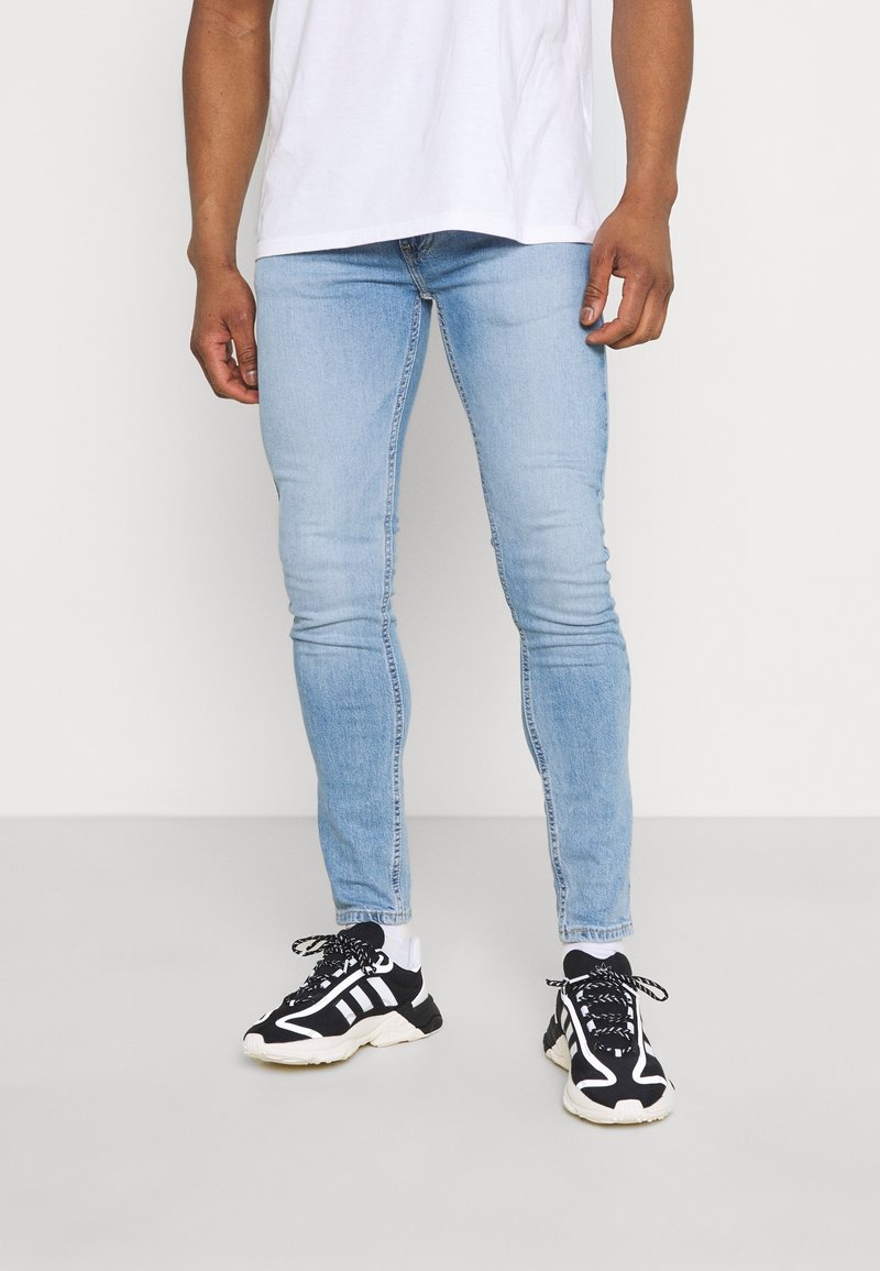 Vaqueros pitillo de mezclilla azul claro, con un diseño clásico de cinco bolsillos y un ligero desgaste. Combinados con zapatillas negras y blancas.