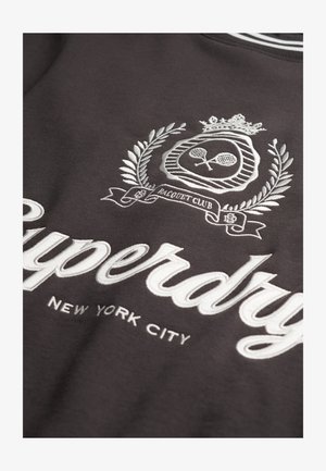 Mørkegrå sweatshirt med hvid broderet tekst "Superdry" og "New York City." Har dekorativt emblem med tennisketsjere og laurbær.