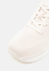 Zapatilla deportiva blanca con un upper texturizado y perforaciones, cordones planos, puntera redondeada y suela acolchada.
