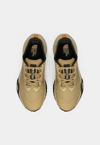 Ταν αθλητικά παπούτσια με επάνω μέρος από δίχτυ, μαύρες λεπτομέρειες, ελαστική σόλα και αντίθετες πορτοκαλί λεπτομέρειες γύρω από τα κορδόνια και τη φτέρνα.