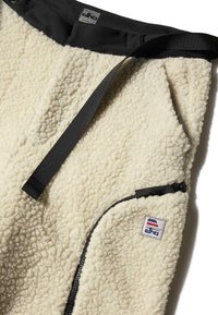 Fleece'owy pulower w kremowym kolorze o teksturowanej, puszystej powierzchni. Posiada czarny kołnierz, kieszeń na zamek oraz łatkę z logo w trzech kolorach.