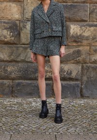Crochet-style two-piece outfit featuring a double-breasted cropped jacket and matching shorts in dark green with multicolored flecks. Black ankle boots.