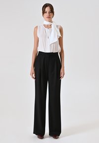 Witte mouwloze blouse met strikdetail, gecombineerd met hoge zwarte wijde broek, gladde stof, zonder patronen of textuur.