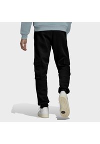 Pantalones cargo negros con bolsillos laterales, puños elásticos y un corte relajado, combinados con zapatillas blancas que cuentan con una suela texturizada.