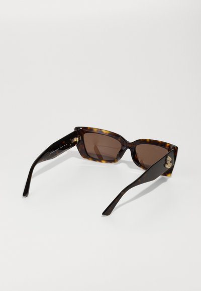 Lunettes de soleil en écaille de tortue avec verres marron, dotées d'une monture géométrique, d'un détail de logo gravé sur le côté et de branches noires élégantes.
