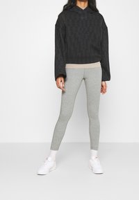 Sudadera negra recortada con textura estampada, combinada con mallas grises y zapatillas blancas. Presenta un corte relajado y capucha.