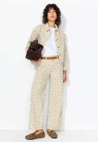 Veste et pantalons beige à motifs avec de petits imprimés floraux, associés à un t-shirt blanc, une ceinture marron, et un sac marron. Mocassins à imprimé léopard.