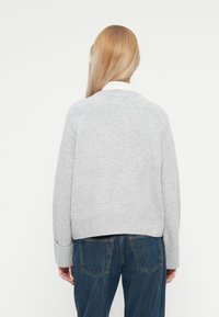 Pull en tricot gris à coupe décontractée, avec des poignets et un ourlet côtelés. La texture semble douce et confortable, associé à un jean en denim bleu.