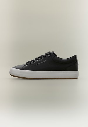 Baskets basses noires avec semelle blanche, lacets noirs et logo Tommy Hilfiger sur le côté, présentées de profil sur un fond neutre.
