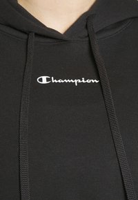 Felpa nera con cappuccio in morbido tessuto e cordini regolabili, con un logo "Champion" bianco ben visibile sul petto.