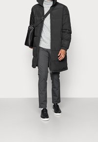 Piumino nero con cappuccio, dolcevita grigio, pantaloni grigi e sneakers nere con suole bianche. Borsa a tracolla in pelle nera.