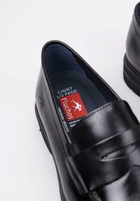 Zwarte leren instappers met een gladde afwerking, met een slip-on ontwerp en een geprofileerde binnenzool met het "Fluchos" logo en verzorgingsinstructies.