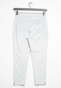 Světlé šedé, slim-fit kalhoty se hladkým povrchem, které mají dvě zadní kapsy a zipy na kotnících. Zobrazeno na černém ramínku.