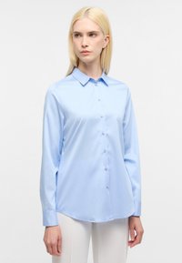 Camicia a maniche lunghe azzurro chiaro con colletto a punta, chiusura frontale con bottoni e texture liscia, dotata di orlo curvo e polsini bottone.