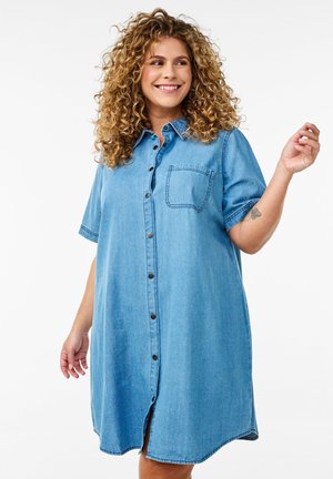 Džínová košeľová šaty svetlomodrej farby, s krátkymi rukávmi, jednou náprsní kapsou a rovnou siluetou s guľatým lemom. Hladká textúra.
