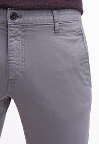 Šedé bavlněné kalhoty s hladkým povrchem, s předním zapínáním na knoflík a bočními kapsami, zdůrazňující štíhlý střih.
