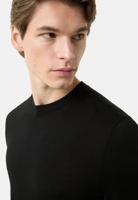 Černý svetr s kulatým výstřihem a žebrovanou texturou, s přiléhavým střihem a hladkým povrchem. Tkanina vypadá lehce a pohodlně.