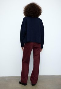 Marineblå cropped sweater lavet af tekstureret stof kombineret med bordeaux vidbenede bukser. Sorte sko fuldender outfittet.