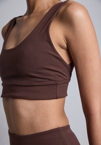 Top de deportista marrón recortado con tirantes anchos y una textura suave, que presenta un diseño ajustado y detalles de costura mínimos.
