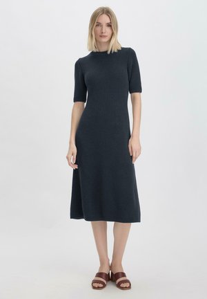 Strickkleid in dunkelblau mit kurzen Ärmeln und gerader Silhouette, mit gerippter Textur und knielangem Saum. Tragen mit braunen Sandalen.