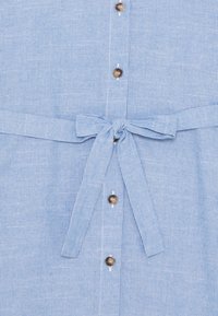 Jasnoniebieska sukienka w paski z przodu na guziki, z brązowymi guzikami i wiązanym paskiem w talii. Tkanina jest miękka z delikatną fakturą.