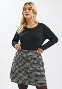 Schwarzes Langarmoberteil kombiniert mit einem strukturierten schwarz-weißen karierten Rock, der fünf Knöpfe vorne und eine ausgestellte Silhouette aufweist.
