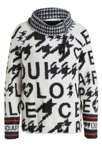 Pull blanc et noir à col montant, avec texte audacieux et motifs d'éclairs. Tissu texturé avec accents rouges et motifs.