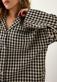 Czarna i kremowa koszula w kratę z guzikami, wykonana z miękkiego materiału, z klasycznym kołnierzykiem, kieszonką z przodu oraz luźnym krojem i szerokimi rękawami.