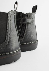 Bottines en cuir noir avec fermeture éclair sur le côté, finition texturée, couture contrastée et semelle en caoutchouc durable.