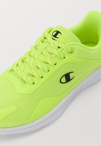 Klart neon-gula sportskor med en texturerad mesh-ovandel, svart logotyp, platta skosnören och en vit gummikjol.