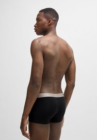 Μαύρα μποξεράκια με μπεζ λάστιχο, κοντά σχέδια και λεία υφή. Το μοντέλο απεικονίζεται από πίσω, επιδεικνύοντας μινιμαλιστικό στιλ.