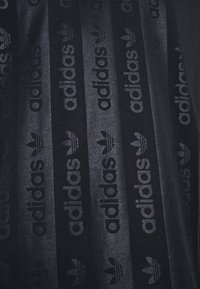 Musta kangas, jonka pinnassa on karkea rakenne, ja se sisältää toistuvia tummanharmaita Adidas-logoja ja kolmi-nauha kuvioita koko suunnittelussa.