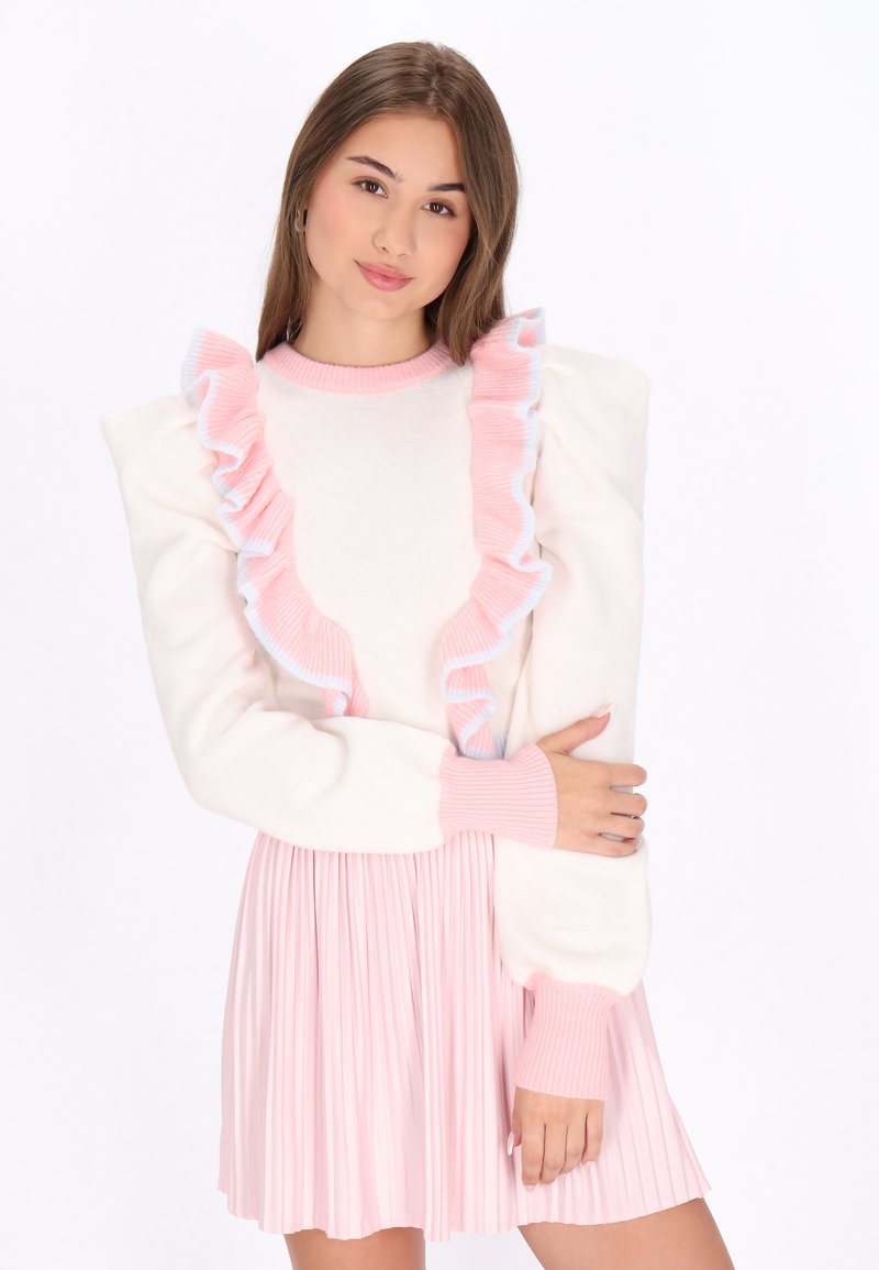 Maglione bianco con dettagli arricciati rosa lungo il collo, abbinato a una gonna plissettata rosa. Il tessuto appare morbido e testurizzato.