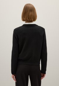 Pull en maille noir avec un col rond, des poignets et un ourlet côtelés. Texture douce, avec une coupe décontractée et des détails au niveau des coutures des épaules.