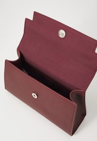 Bordó clutch laukku, joka on valmistettu teksturoidusta materiaalista, jossa on hopeinen painonappi ja avoin sisustus kaarevilla sivureunoilla.